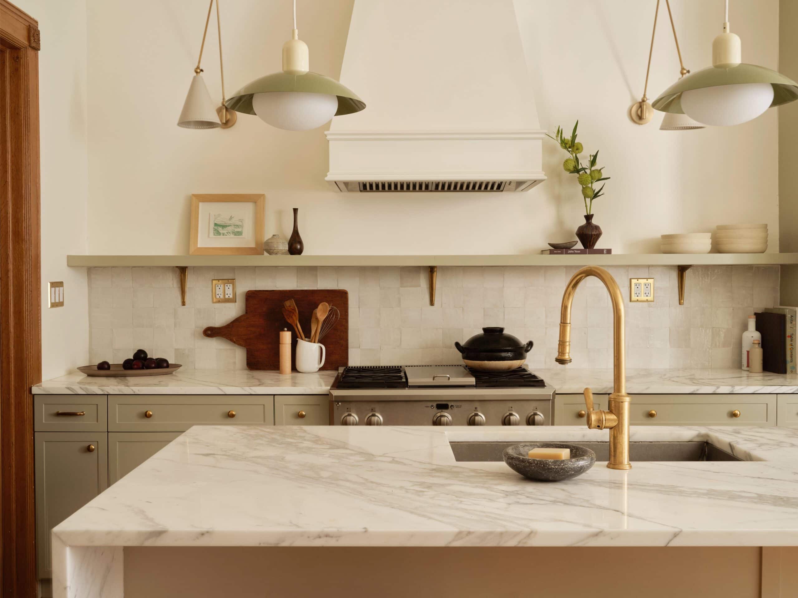 Modern kitchen with marble countertops, brass faucet, gas stove, open shelves with dishes, and pendant lights hanging from the ceiling.