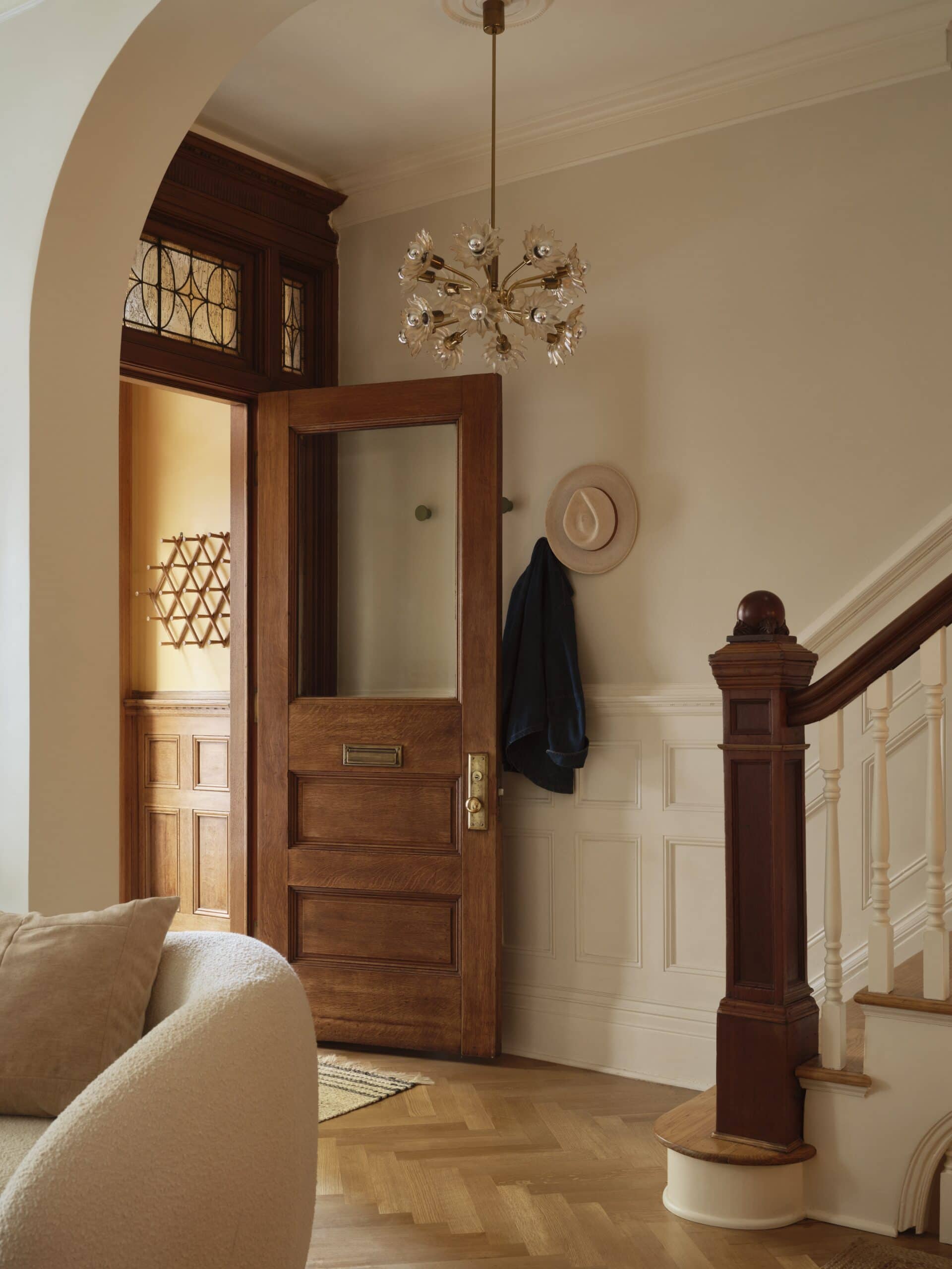Entryway with a wooden front door, coat and hat hanging on hooks, a staircase with wooden railing, chandelier, and white wainscoting on the walls.