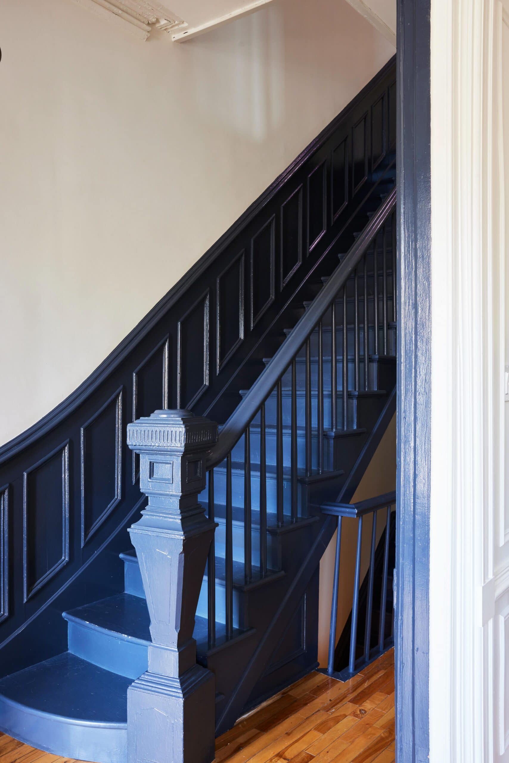 A dark blue-painted wooden staircase with a matching banister, set against light-colored walls and a polished wood floor.