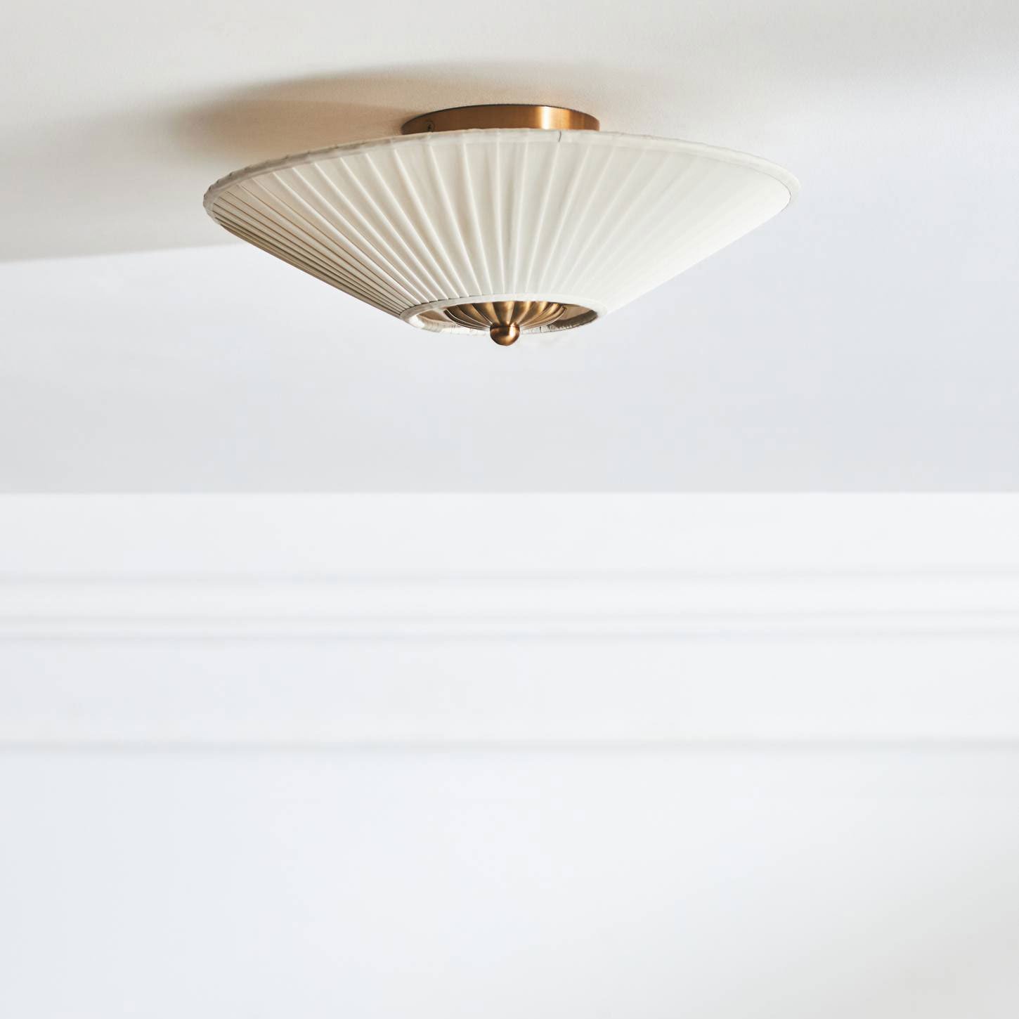 A white fluted ceiling light fixture with brass accents is mounted on a white ceiling.